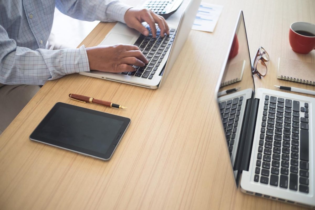 Person working on a laptop beside documents and another laptop