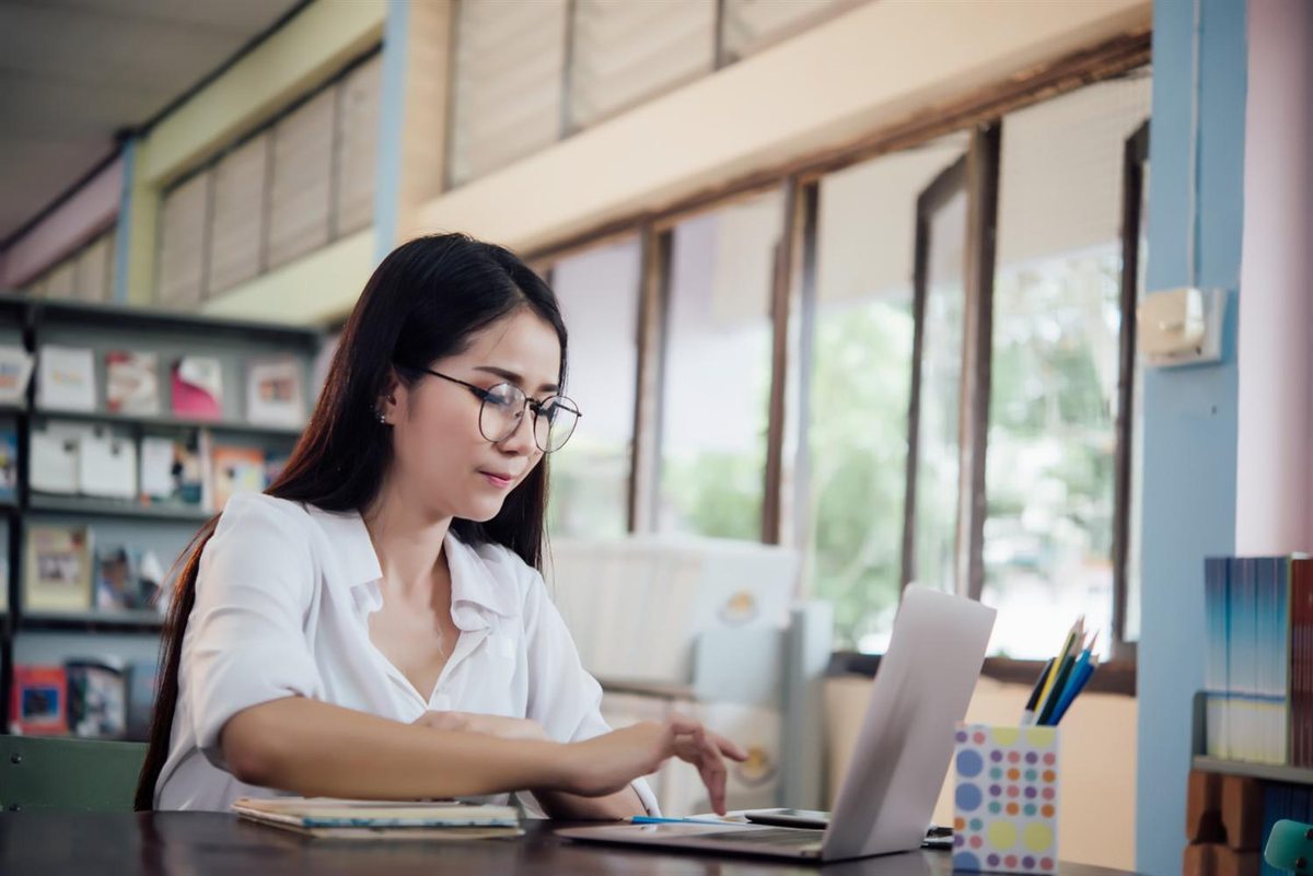 Student using a laptop beside bookshelves