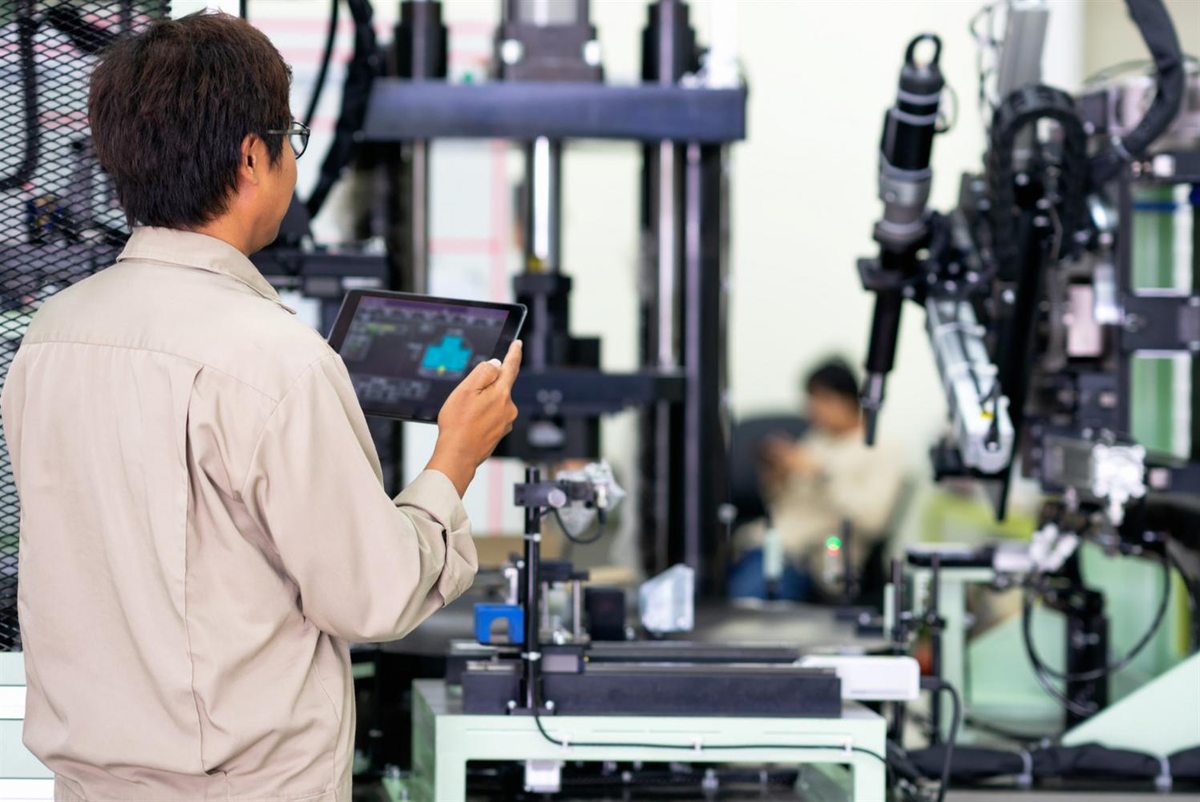 Technician using a tablet beside factory machinery