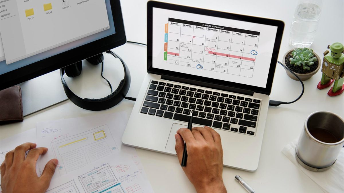 Laptop displaying a calendar beside planning notes