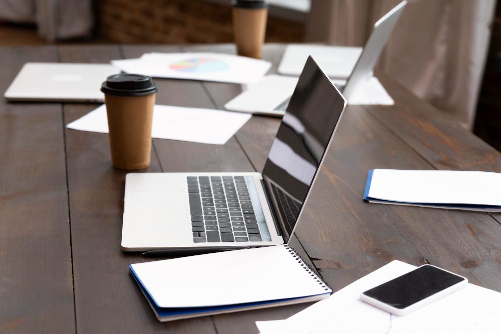 Laptop, notebooks, phone, and takeaway cup on a desk