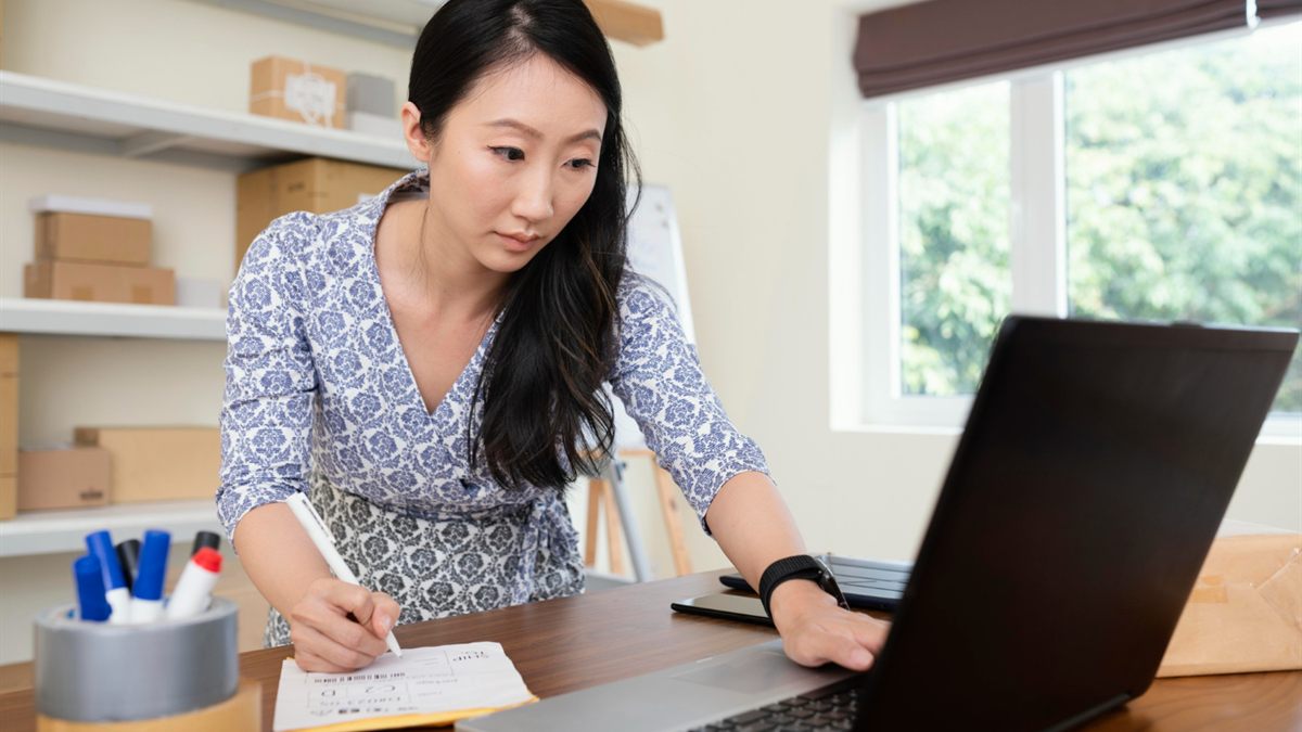 Woman writing in a notebook beside an open laptop